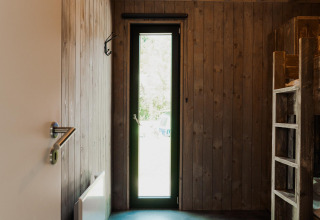Camera rivestita in legno con letti a castello e stretta porta a vetri, tipica alloggio in stile glamping.