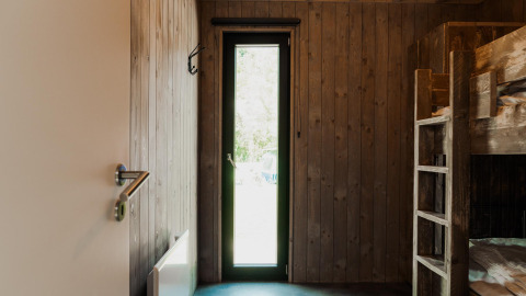 Habitación con paneles de madera, literas y puerta de cristal estrecha, típica de un alojamiento glamping.