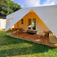 Tenda safari con veranda in legno, panchine e tavolo da picnic su prato verde in area campeggio.
