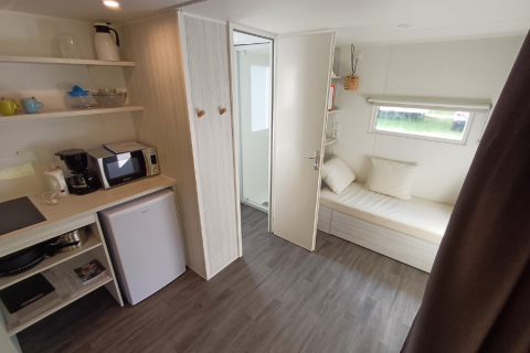 Interieur van een safaritent met kitchenette, minikoelkast, microgolfoven en slaapbank bij het raam.