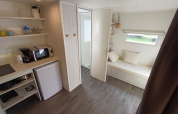 Interieur van een safaritent met kitchenette, minikoelkast, microgolfoven en slaapbank bij het raam.
