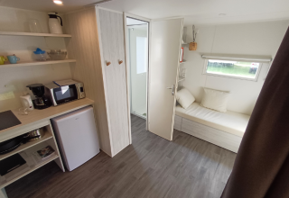 Interieur van een safaritent met kitchenette, minikoelkast, microgolfoven en slaapbank bij het raam.