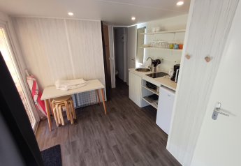Interieur van safaritent met kitchenette, kleine koelkast, tafel, krukjes, gootsteen en open planken.