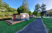 Foto di una tenda safari con veranda in legno su un campeggio, circondata da erba e alberi verdi.