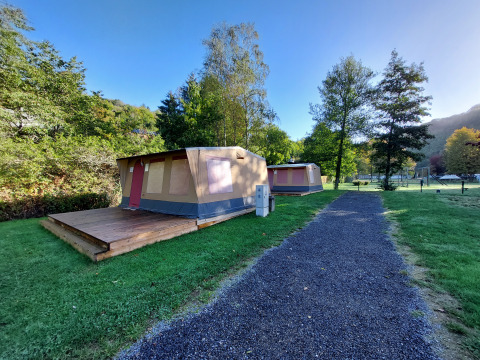 Foto di una tenda safari con veranda in legno su un campeggio, circondata da erba e alberi verdi.