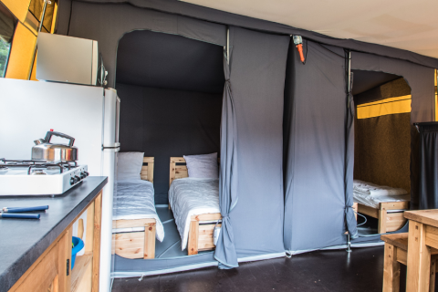 Interno di una tenda safari con due letti singoli, angolo cottura, frigorifero e tavolo in legno.