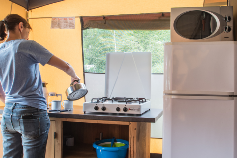 Persona prepara il caffè su fornello a gas nella cucina di una tenda safari con frigo e microonde.