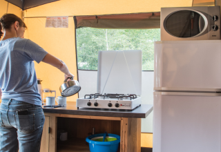 Persona prepara il caffè su fornello a gas nella cucina di una tenda safari con frigo e microonde.