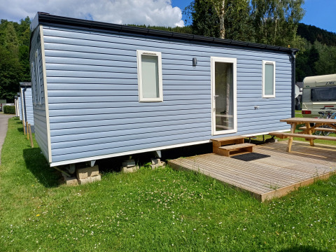 Cabaña azul de glamping moderna con terraza, pequeños escalones y mesa de picnic sobre césped verde.