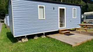 Modern blue glamping cabin with small steps, wooden deck, and picnic table on green grass outdoors.