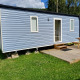 Casa mobile blu moderna con terrazza in legno, gradini e tavolo da picnic su prato verde in campeggio.