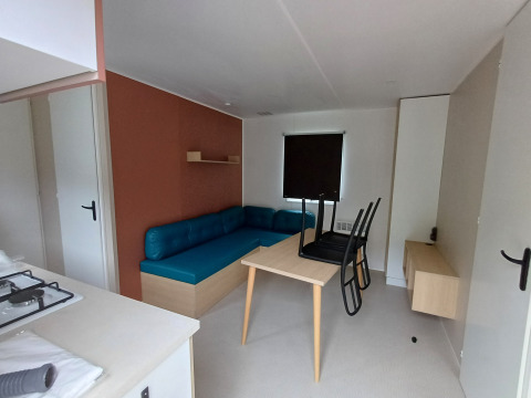 Alojamiento glamping moderno con sofá azul, mesa, sillas y pequeña zona de cocina luminosa.