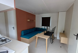 Sistemazione glamping moderna con divano blu, tavolo da pranzo, sedie e piccolo angolo cottura.