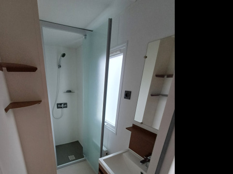 Bagno moderno in alloggio glamping con doccia, lavabo e ampia finestra che lascia entrare la luce.