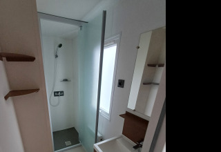 Bagno moderno in alloggio glamping con doccia, lavabo e ampia finestra che lascia entrare la luce.