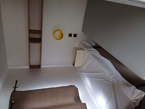 Una camera di glamping con letto singolo, lenzuolo bianco, mensole, specchio tondo giallo e tenda marrone.