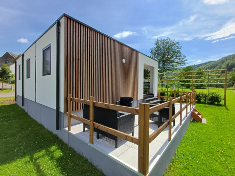 Moderne glamping accommodatie met terras, buitenzitje en zicht op groene natuur en bomen.