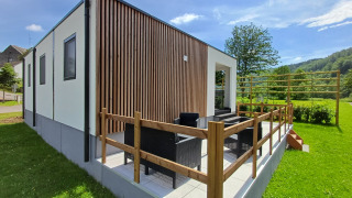 Struttura glamping moderna con terrazza, area salotto all'aperto e vista su un paesaggio verde e naturale.
