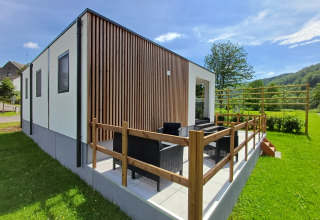 Moderne Glamping-Unterkunft mit Terrasse, Sitzbereich im Freien und Blick auf grüne Natur und Bäume.