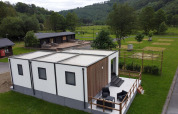 Alloggio glamping moderno con terrazza e posti a sedere all'aperto in un ambiente verde e naturale.