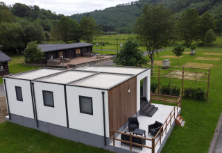Alloggio glamping moderno con terrazza e posti a sedere all'aperto in un ambiente verde e naturale.