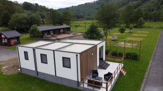 Modernes Glamping-Unterkunft mit Terrasse und Sitzplätzen im Freien in grüner Umgebung.