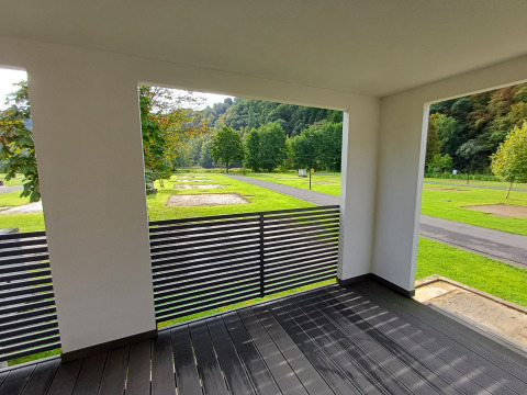 Zicht vanuit een moderne glampingaccommodatie met terras over groene grasvelden en bomen.