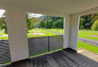 Zicht vanuit een moderne glampingaccommodatie met terras over groene grasvelden en bomen.