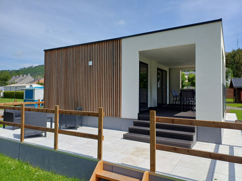 Alloggio glamping moderno con rivestimento in legno, terrazza esterna e area coperta per sedersi e rilassarsi.