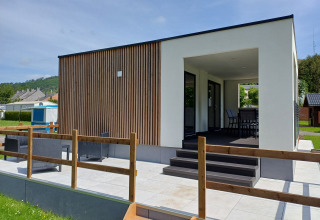 Alloggio glamping moderno con rivestimento in legno, terrazza esterna e area coperta per sedersi e rilassarsi.