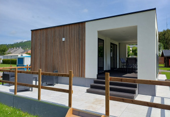 Alloggio glamping moderno con rivestimento in legno, terrazza esterna e area coperta per sedersi e rilassarsi.