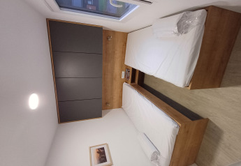 Modern glamping room with two single beds, wooden furniture, a large window, and dark wall cabinets.