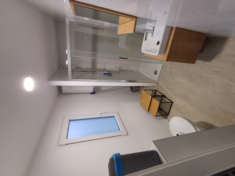 Modern glampingbadkamer met douche, venster, wastafel, houten vloer en minimalistisch meubilair.