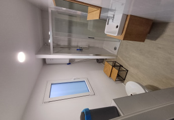 Modern bathroom in glamping accommodation with shower, window, small sink and wooden furniture.