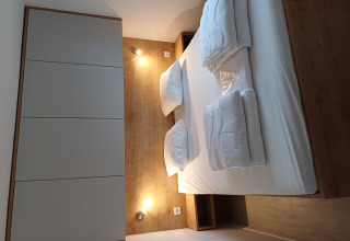 Alloggio glamping moderno con letto matrimoniale, parete in legno, biancheria e illuminazione soffusa.