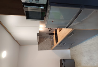 Moderne keukenhoek met kookplaat, oven, koelkast en spoelbak in een glampingverblijf.