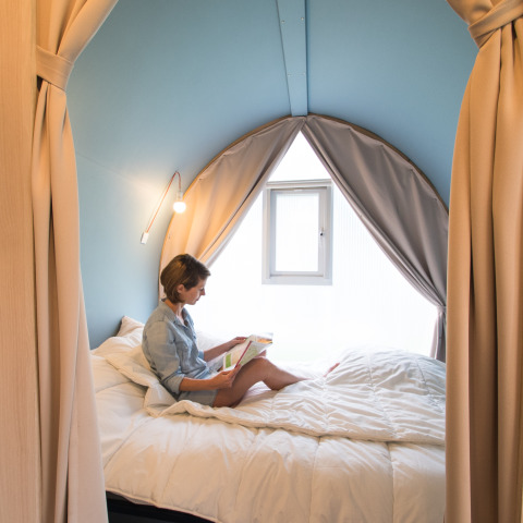 Mujer leyendo un libro dentro de la tienda safari Coco Sweet en Camping La Colline, Bélgica, ambiente acogedor.
