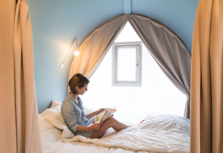 Mujer leyendo un libro dentro de la tienda safari Coco Sweet en Camping La Colline, Bélgica, ambiente acogedor.