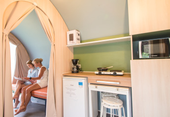 Interno della tenda safari Coco Sweet al Camping La Colline in Belgio con due donne, angolo cucina e seduta.