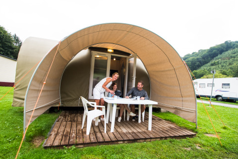 Gezin geniet van een maaltijd voor een Coco Sweet safari tent op een camping met groene omgeving.