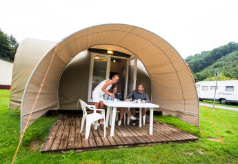 Gezin eet samen voor een Coco Sweet safaritent op een camping met veel groen en heuvels rondom.