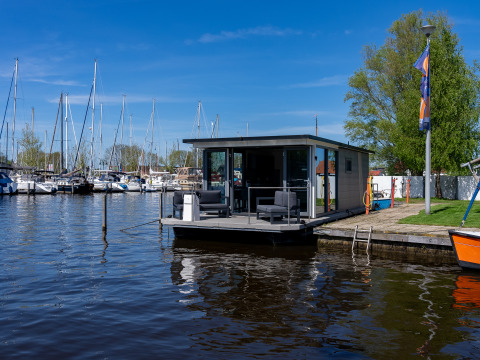 Moderne husbåd Houseboat Heeg fortøjet ved Marina Heeg i Holland med lystbåde i baggrunden.