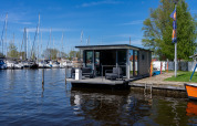 Modern Houseboat Heeg moored at Marina Heeg in the Netherlands with yachts and blue skies in the background.