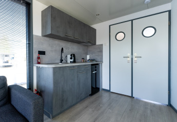 Moderne kitchenette i Houseboat Heeg med grå skabe, tekande og lys, placeret ved Marina Heeg, Holland.