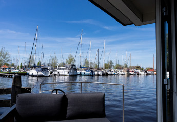 Blick von Houseboat Heeg in Marina Heeg, Niederlande, mit Sofa und Segelbooten bei blauem Himmel.