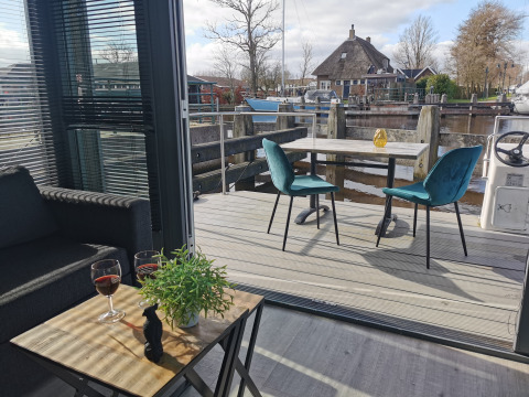 Vue de Houseboat Heeg à Marina Heeg, Pays-Bas, avec terrasse, table et chaises le long de l’eau.