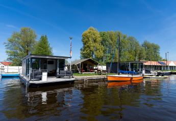 Houseboat at Marina Heeg in the Netherlands, docked on the water with boats and trees in the background.
