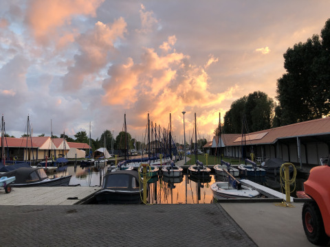 Sunset at Marina Heeg in the Netherlands, showing boats moored by houseboats and a dramatic sky above.