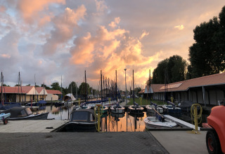 Solnedgang over marinaen i Heeg, Holland, med både ved kajen og idylliske husbåde langs vandet.