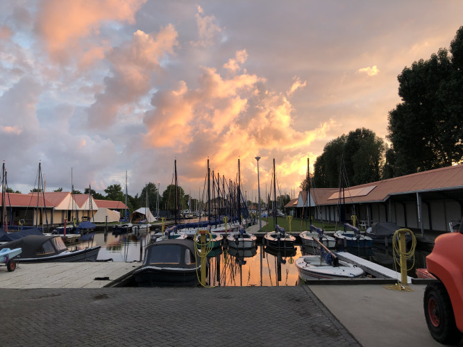 Atardecer en Marina Heeg en Países Bajos, con barcos amarrados y una casa flotante bajo un cielo colorido.